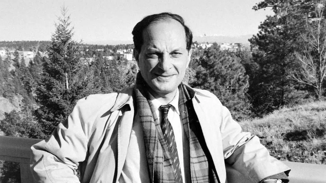 A man in a jacket and tie standing on top of a hill.