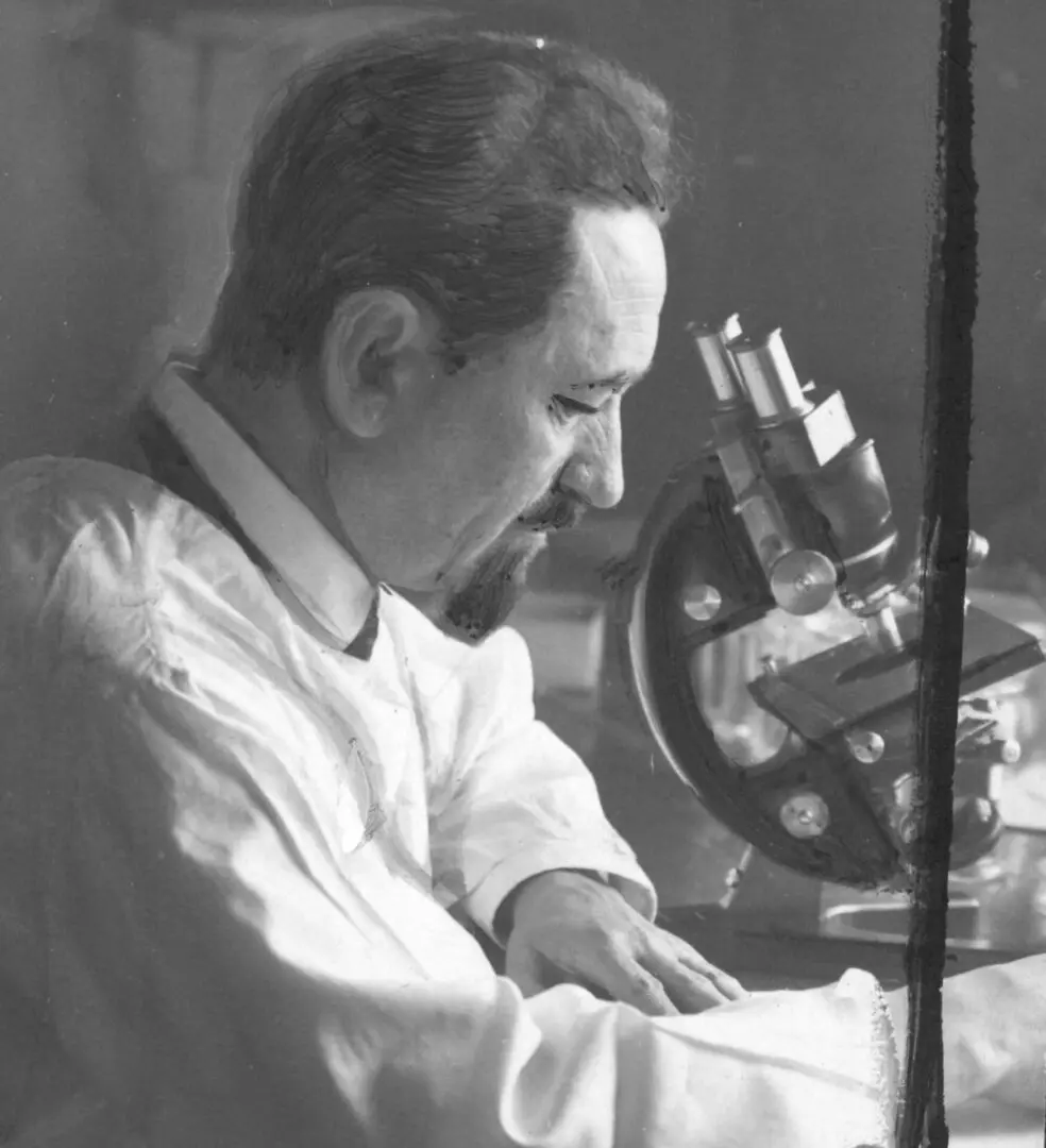 A man in white shirt working with a microscope.