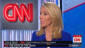 A cnn anchor is sitting in front of the cnn logo.
