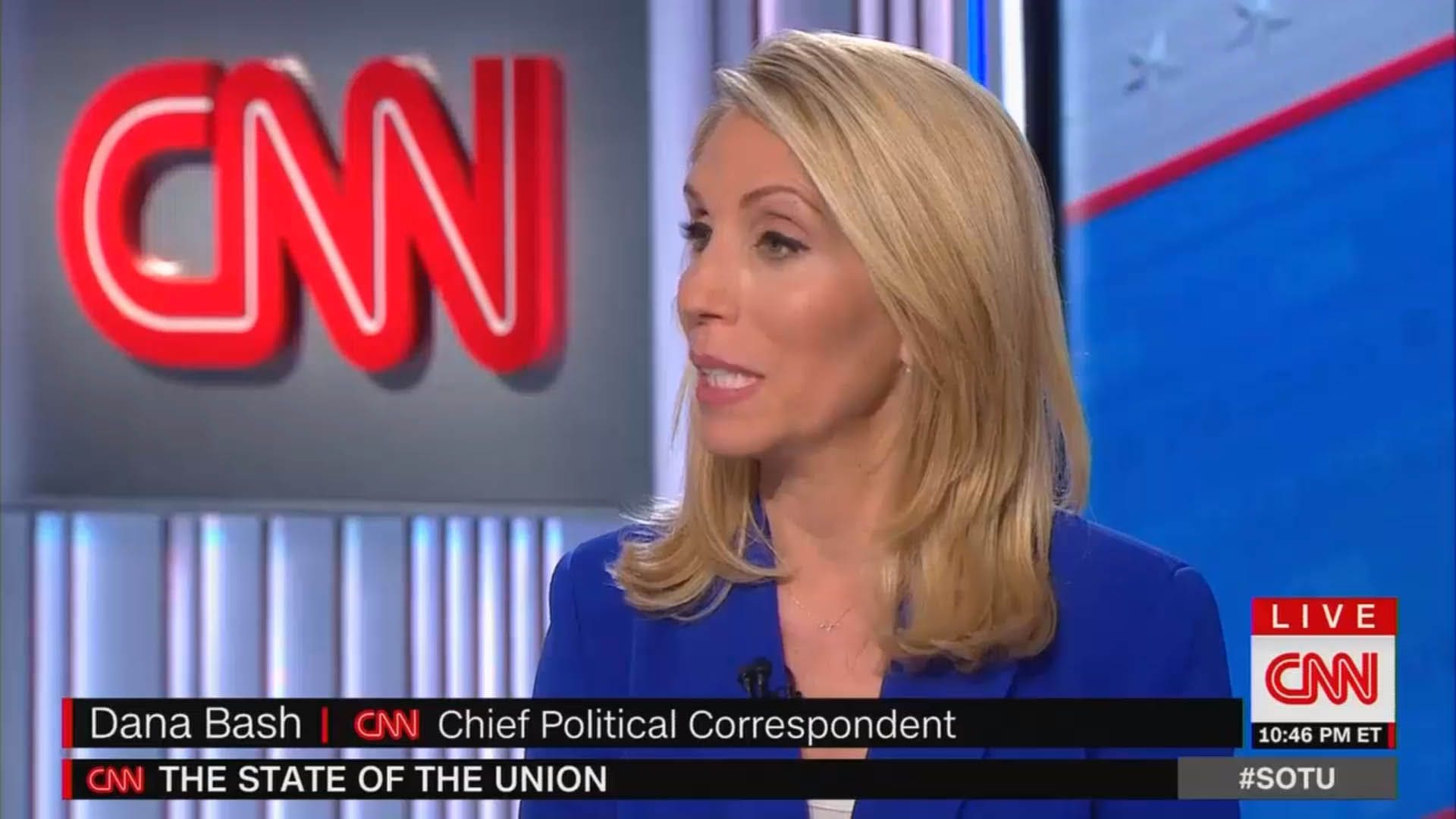A cnn anchor is sitting in front of the cnn logo.