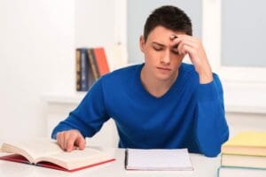 Young man studying at a desk with books.