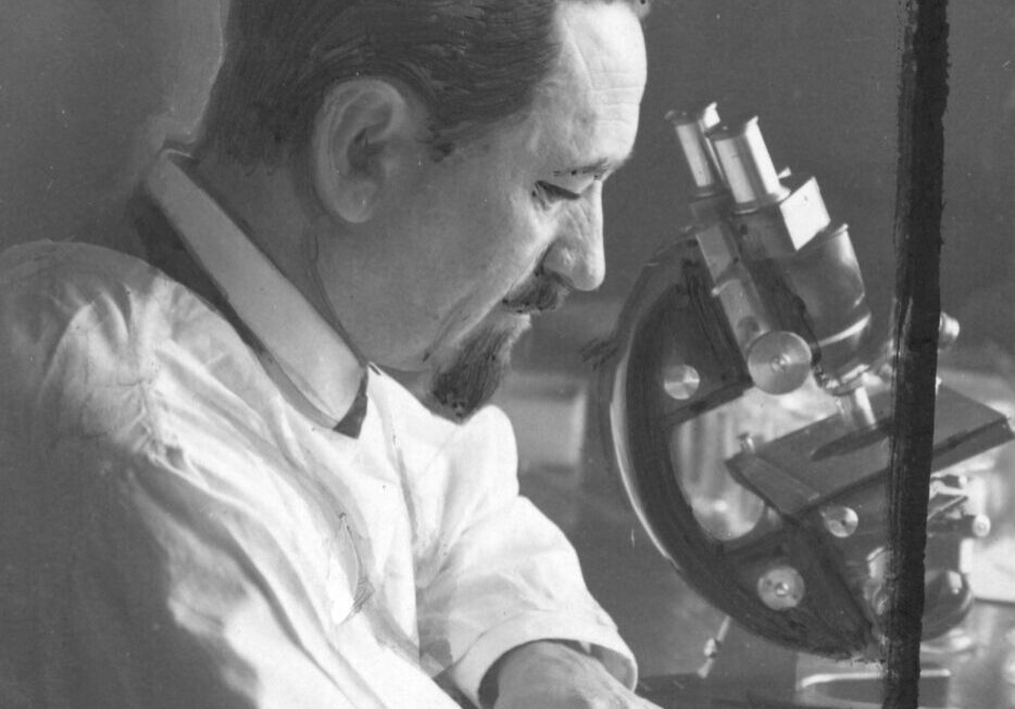 A man in white shirt working with a microscope.