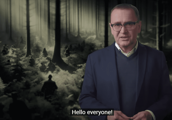 Man in suit speaking in front of forest.